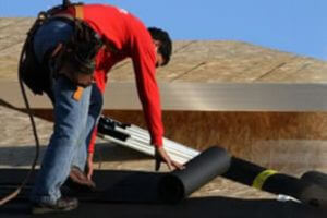 roofing contractor on wooden roof rolling out roofing materials