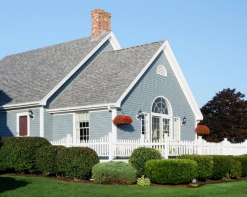 exterior residential home with green landscaping, blue vinyl siding, and shingle roofing