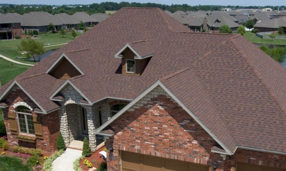 reddish brown asphalt shingle roof installed over a large home and attached 3 car garage with brick siding